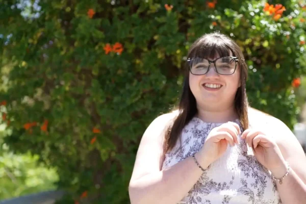 Young woman smiling in the sunshine outside in front of greenery with flowers