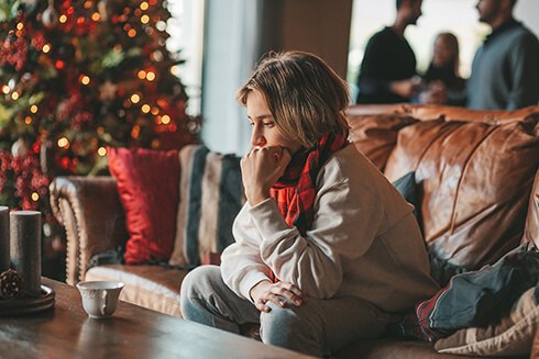 Woman sitting on leather sofa looking anxious with holiday decorations in background
