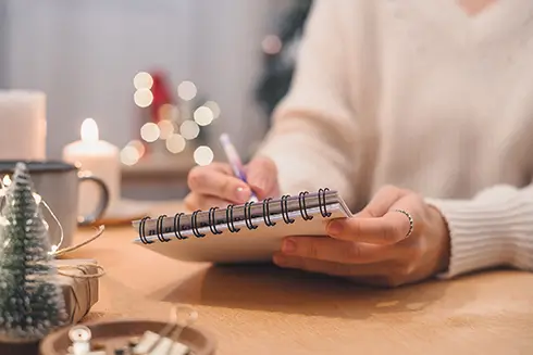 Woman sitting at desk writing in notebook with holiday decorations in background
