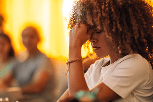 Woman sitting with eyes closed and fist to her forehead looking frustrated