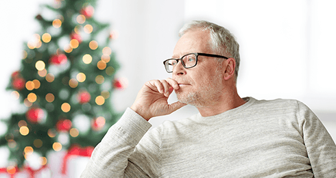 Older man sitting on couch in front of holiday decorations looking pensive