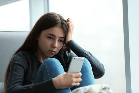 Sad teen girl looking at smartphone while being cyberbullied
