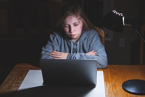 Sad teen girl looking at laptop in the dark with her arms folded