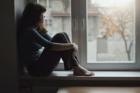 Sad woman sitting on window seat looking out window at dreary winter day
