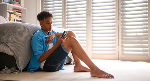 Teen boy sitting on bedroom floor looking at phone