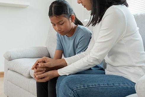 Teen girl sitting on sofa with her mom being comforted